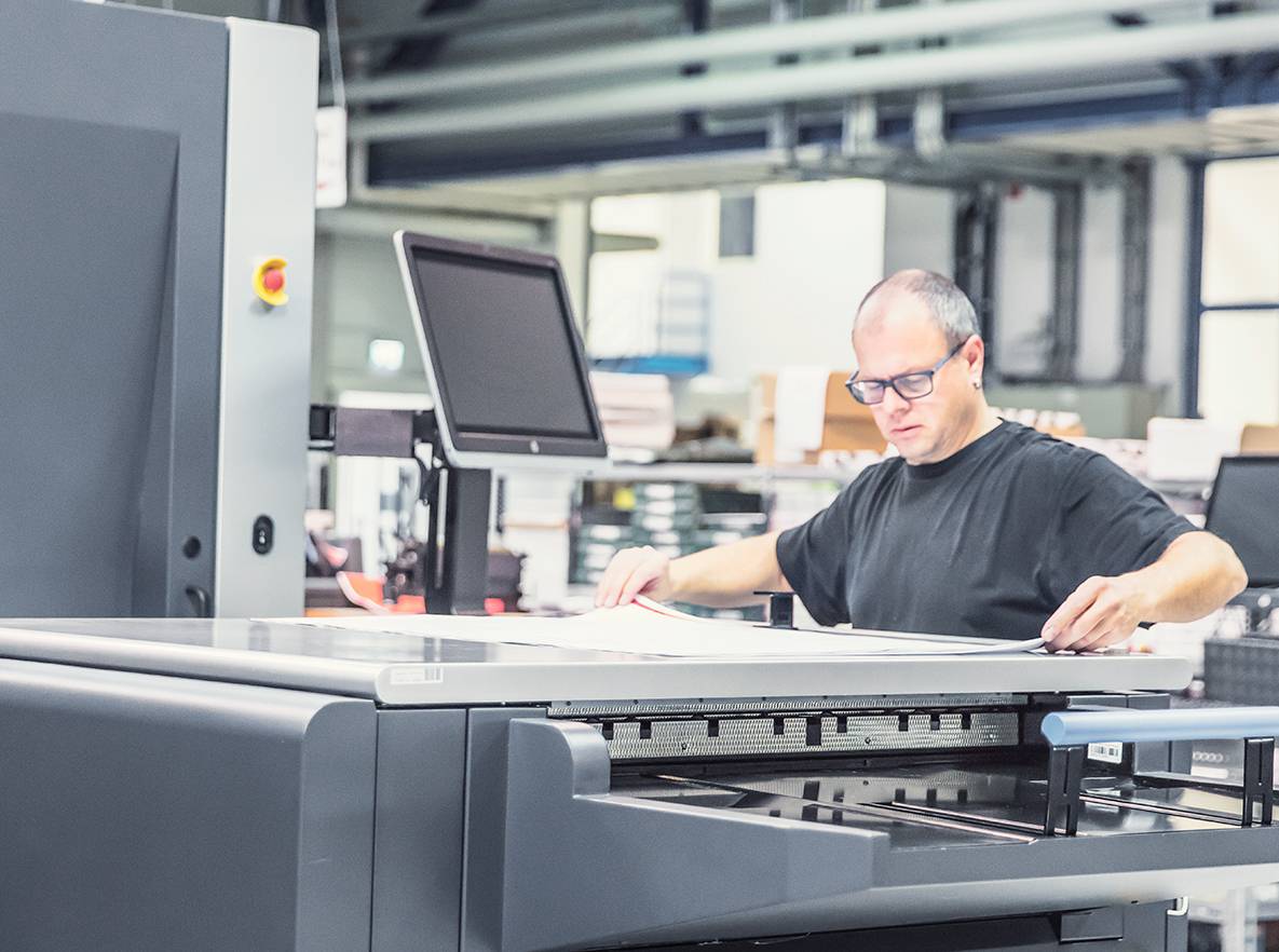 Mitarbeiter prüft einen frisch gedruckten Bogen an der Digitaldruckmaschine